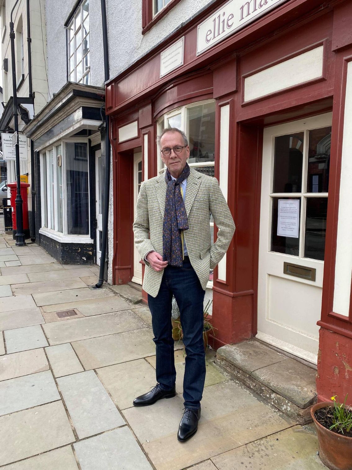 Man in a beige jacket and black trousers in front of Ellie's store